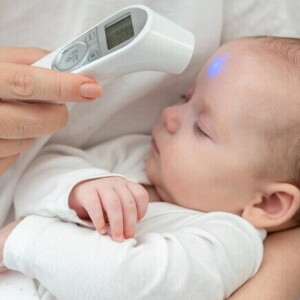 Uma mão medindo a temperatura do bebê com termômetro digital na testa.