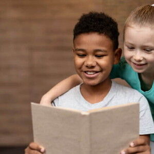 Duas crianças sorrindo, lendo um livro juntas.