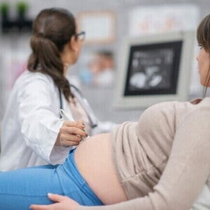 Uma mulher grávida deitada enquanto uma profissional de saúde realiza um ultrassom abdominal. Uma mulher grávida deitada enquanto uma profissional de saúde realiza um ultrassom abdominal.