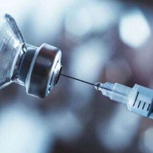 Imagem de uma seringa de vacina e um frasco de medicamento sob um fundo desfocado
