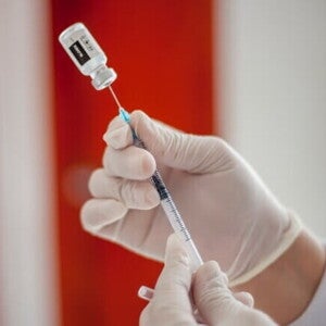 Profissional de saúde com luvas preparando uma seringa com uma dose de vacina retirada de um frasco. Profissional de saúde com luvas preparando uma seringa com uma dose de vacina retirada de um frasco.