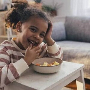 Foto de uma criança fazendo um lanche e comendo com as mãos uma vasilha de salada de frutas, um exemplo de alimento rico em vitamina C