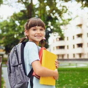 Uma menina sorrindo, segurando o material escolar e vestindo uniforme