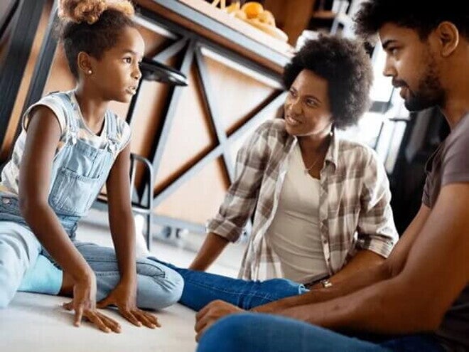 Pai e mãe estão sentado nos chão e conversam com sua filha, uma criança de 5 anos. Pai e mãe estão sentado nos chão e conversam com sua filha, uma criança de 5 anos.