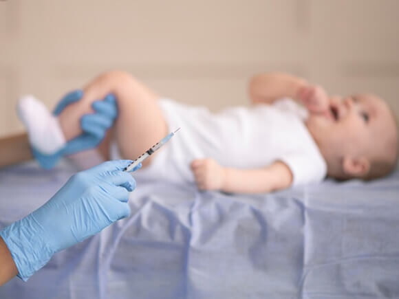 bebê deitado e enfermeira segurando uma seringa