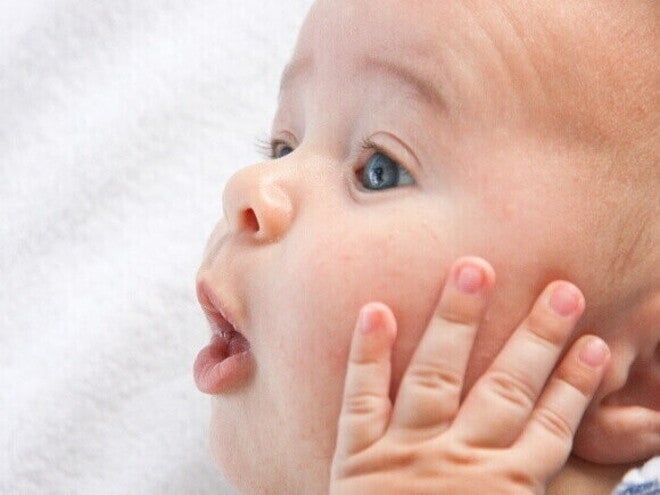 Um close-up do rosto de um bebê, com a boca ligeiramente aberta e a mão levantada perto do rosto. Um close-up do rosto de um bebê, com a boca ligeiramente aberta e a mão levantada perto do rosto.