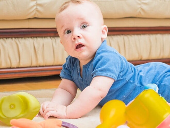 Bebê deitado de bruços no chão com alguns brinquedos em sua volta Bebê deitado de bruços no chão com alguns brinquedos em sua volta