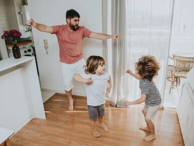 Pai e filhos pequenos brincam desenvolvendo a coordenação motora grossa dentro de casa. Pai e filhos pequenos brincam desenvolvendo a coordenação motora grossa dentro de casa.