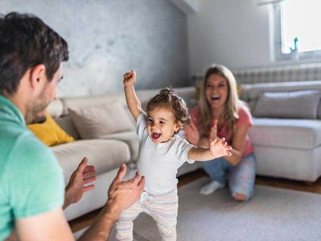 Pai e mãe em um momento feliz auxiliando nos primeiros passos da bebê. Pai e mãe em um momento feliz auxiliando nos primeiros passos da bebê.