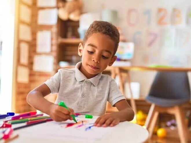 Uma criança de 4 anos está em uma sala de aula, sentado à mesa, e usa uma caneta hidrocor para desenhar Uma criança de 4 anos está em uma sala de aula, sentado à mesa, e usa uma caneta hidrocor para desenhar