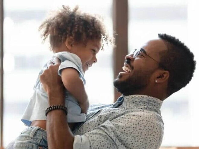 Uma criança é carregada pelo seu pai. Os dois estão brincando e sorrindo. A imagem remete ao tema crise dos três anos Uma criança é carregada pelo seu pai. Os dois estão brincando e sorrindo. A imagem remete ao tema crise dos três anos