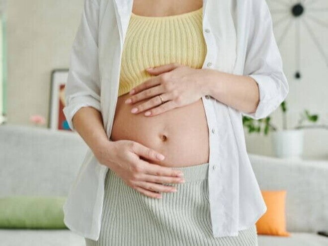Uma mulher grávida em pé, com as duas mãos sobre a barriga. Uma mulher grávida em pé, com as duas mãos sobre a barriga.