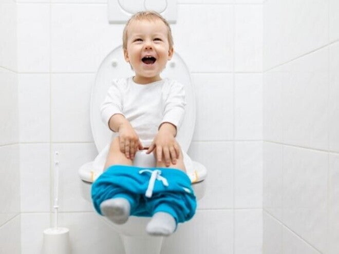 Uma criança sentada em um vaso sanitário com os shorts abaixados, rindo e olhando para cima, em um banheiro. Uma criança sentada em um vaso sanitário com os shorts abaixados, rindo e olhando para cima, em um banheiro.