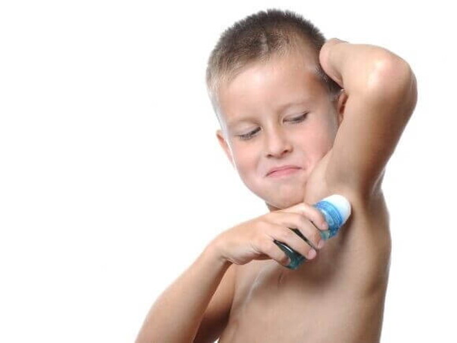 Menino utilizando um desodorante em formato roll-on sob um fundo branco. Menino utilizando um desodorante em formato roll-on sob um fundo branco.