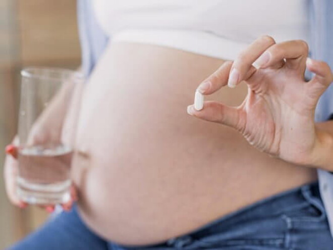 Mulher grávida segurando um copo de água em uma mão e uma cápsula de suplemento na outra mão Mulher grávida segurando um copo de água em uma mão e uma cápsula de suplemento na outra mão