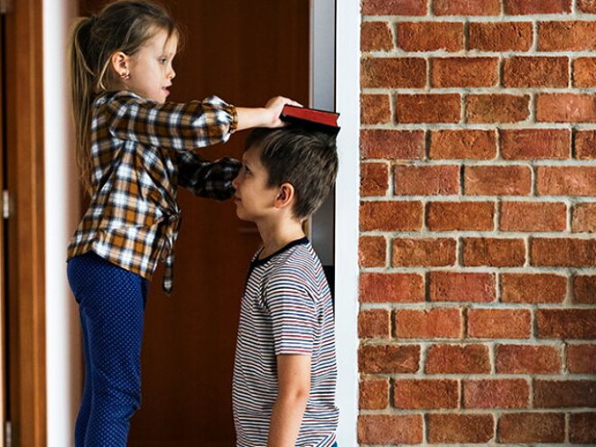 Duas crianças em frente um parede de tijolos brincando de medir a altura Duas crianças em frente um parede de tijolos brincando de medir a altura
