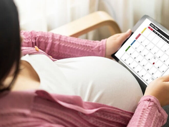 Gestante sentando em uma cadeira olhando para um calendário virtual Gestante sentando em uma cadeira olhando para um calendário virtual