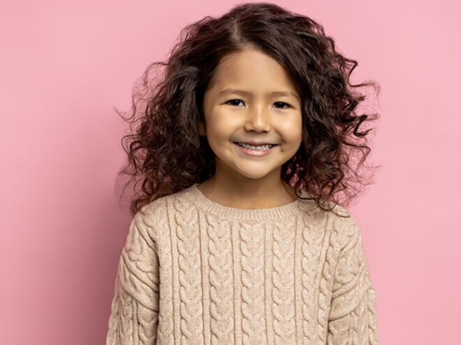 Menina de cabelo ondulado sorrindo em frente a uma parede cor de rosa. Menina de cabelo ondulado sorrindo em frente a uma parede cor de rosa.