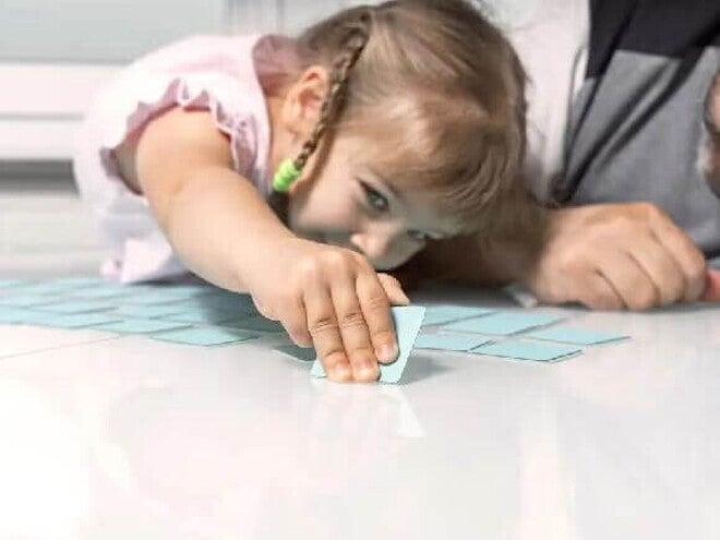 Jogos educativos Uma menina e um adulto brincam de jogo de memória, um dos tipos de jogos educativos.