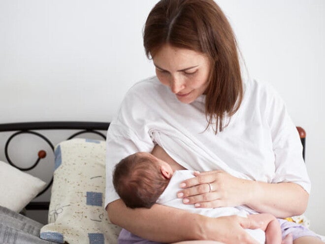 mãe amamenta bebê sentada em cama