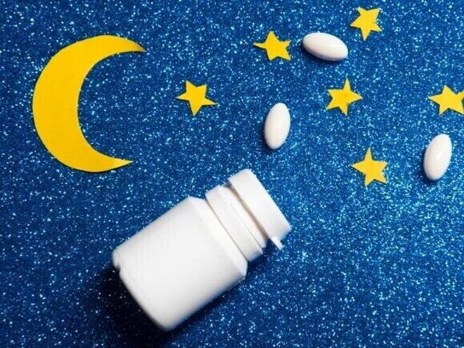 Frasco branco de comprimidos aberto com pílulas espalhadas sobre fundo azul com brilho, decorado com estrelas e uma lua amarela de papel. Frasco branco de comprimidos aberto com pílulas espalhadas sobre fundo azul com brilho, decorado com estrelas e uma lua amarela de papel.