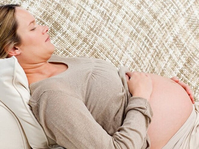 Mulher grávida deitada no sofá embalando sua barriga Mulher grávida deitada no sofá embalando sua barriga
