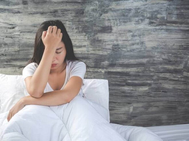 mulher sentada em cama com lençóis brancos enquanto está cabisbaixa. mulher sentada em cama com lençóis brancos enquanto está cabisbaixa.