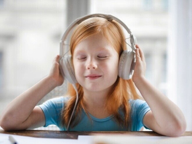 Uma menina de olhos fechados, usando fones de ouvido e sorrindo levemente, com as mãos próximas aos fones. Uma menina de olhos fechados, usando fones de ouvido e sorrindo levemente, com as mãos próximas aos fones.