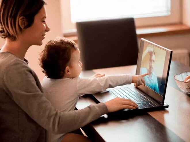 Ilustrando a separação dos pais, uma mãe segura um bebê em seu colo. Eles estão sentados à mesa em frente ao computador. O bebê aponta para a tela, onde há um homem por videochamada. Ilustrando a separação dos pais, uma mãe segura um bebê em seu colo. Eles estão sentados à mesa em frente ao computador. O bebê aponta para a tela, onde há um homem por videochamada.