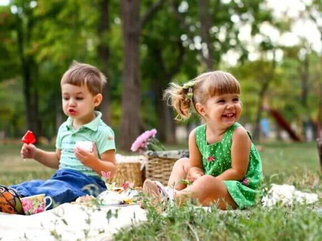 Piquenique infantil Um menino e uma menina estão sentados em uma toalha em um parque. Sobre ela temos algumas cestas e lanchinhos. O cenário todo remete muito a um dia de piquenique