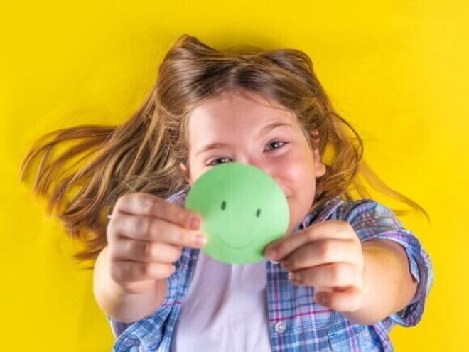 Uma criança deitada e sorrindo, segurando um círculo de papel verde com um rosto sorridente desenhado. Uma criança deitada e sorrindo, segurando um círculo de papel verde com um rosto sorridente desenhado.