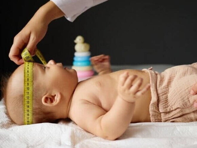 Um bebê deitado, com a cabeça sendo medida por outra pessoa com uma fita métrica. Um bebê deitado, com a cabeça sendo medida por outra pessoa com uma fita métrica.