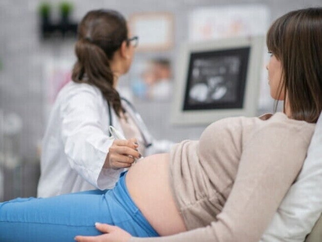 Uma mulher grávida deitada enquanto uma profissional de saúde realiza um ultrassom abdominal. Uma mulher grávida deitada enquanto uma profissional de saúde realiza um ultrassom abdominal.