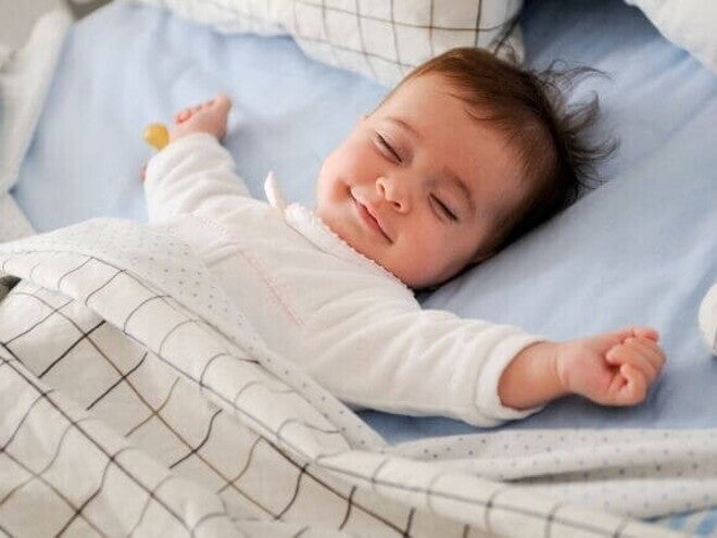 Bebê dormindo de barriga para cima em uma cama com lençóis e cobertor, transmitindo sensação de conforto e tranquilidade. Bebê dormindo de barriga para cima em uma cama com lençóis e cobertor, transmitindo sensação de conforto e tranquilidade.