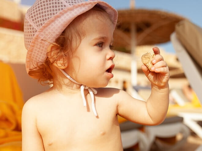 Criança de olhos claros sentado na areia da praia usando chapéu para se proteger do sol. Criança de olhos claros sentado na areia da praia usando chapéu para se proteger do sol.