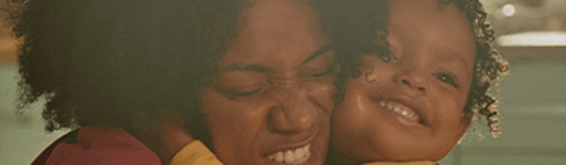 Mãe, com os olhos fechados, abraça a filha de três anos na cozinha de casa. Mãe, com os olhos fechados, abraça a filha de três anos na cozinha de casa.