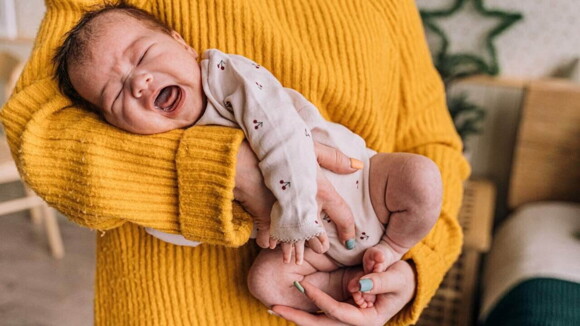 Close em um bebê chorando no colo de uma mulher usando roupa de cor amarela. Close em um bebê chorando no colo de uma mulher usando roupa de cor amarela.