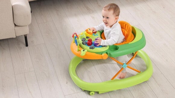 Bebê sentado em um andador colorido com brinquedos, em uma sala com piso de madeira clara. Bebê sentado em um andador colorido com brinquedos, em uma sala com piso de madeira clara.