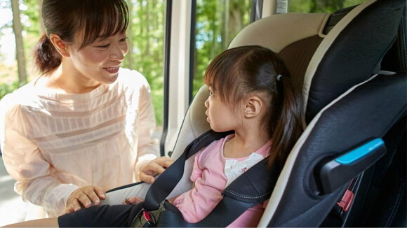 Uma mãe sorrindo e interagindo com sua filha pequena, que está sentada em uma cadeirinha infantil dentro de um carro. Uma mãe sorrindo e interagindo com sua filha pequena, que está sentada em uma cadeirinha infantil dentro de um carro.