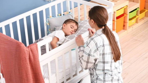 Uma babá observa uma criança dormindo no berço Uma babá observa uma criança dormindo no berço