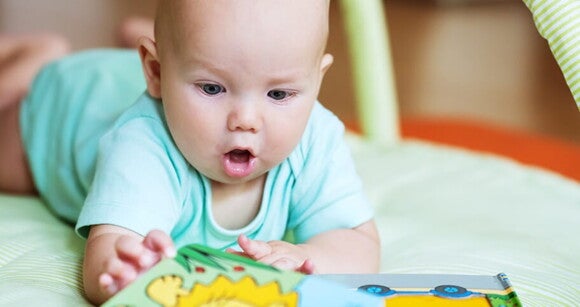 Bebê de bruços tentando pegar um livrinho que está na sua frente Bebê de bruços tentando pegar um livrinho que está na sua frente