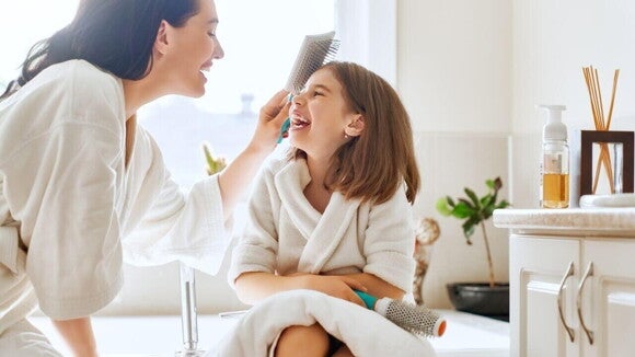 Mulher e criança sorrindo, enquanto a mulher escova o cabelo da criança em um banheiro bem iluminado. Mulher e criança sorrindo, enquanto a mulher escova o cabelo da criança em um banheiro bem iluminado.