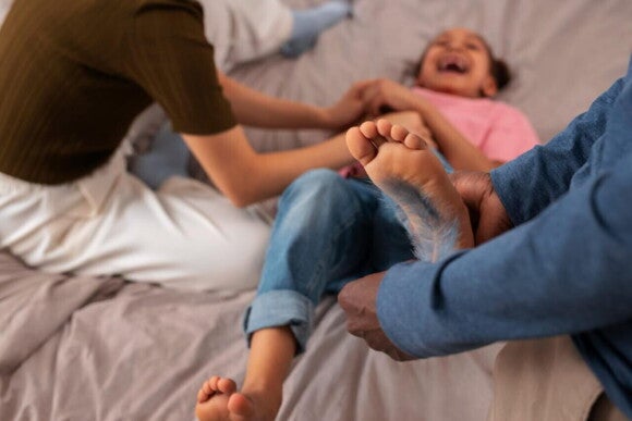 Criança deitada e rindo, enquanto duas pessoas fazem cócegas em diferentes partes do seu corpo. Criança deitada e rindo, enquanto duas pessoas fazem cócegas em diferentes partes do seu corpo.