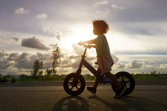 Foto de criança andando de bicicleta usando os pés como apoio. 