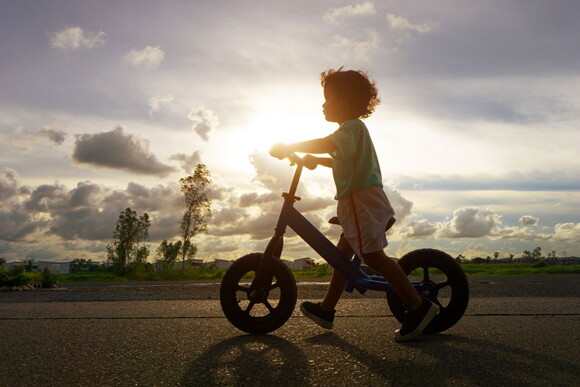 Tem uma idade certa para começar a andar de bicicleta? Foto de criança andando de bicicleta usando os pés como apoio.