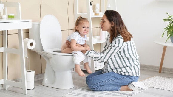 Uma mulher ajoelhada segura uma criança que chora sentada em um vaso sanitário em um banheiro. Uma mulher ajoelhada segura uma criança que chora sentada em um vaso sanitário em um banheiro.