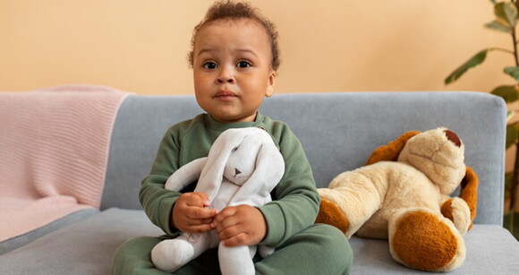 Bebê de cabelo cacheado sentado no sofá usando pijama e abraçando seus ursinhos de pelúcia. Bebê de cabelo cacheado sentado no sofá usando pijama e abraçando seus ursinhos de pelúcia.