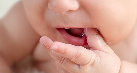 Foto focada no rosto do bebê que está com a mãozinha na boca