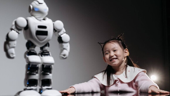 Menina sorrindo ao lado de um robô branco em um ambiente digital. Menina sorrindo ao lado de um robô branco em um ambiente digital.