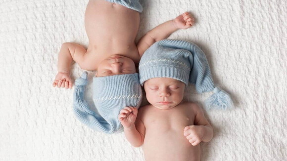 Dois bebês deitados lado a lado em uma cama, vestindo toucas iguais. Dois bebês deitados lado a lado em uma cama, vestindo toucas iguais.